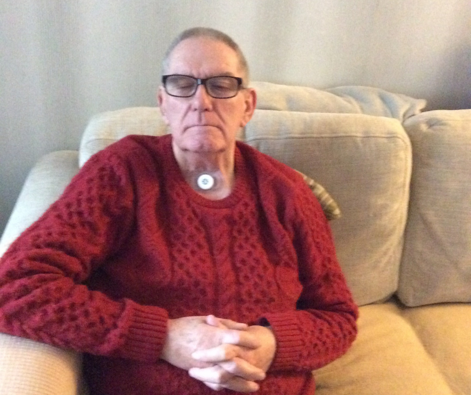 Malcolm sat on a sofa wearing a red jumper and Provox Life Energy HME.